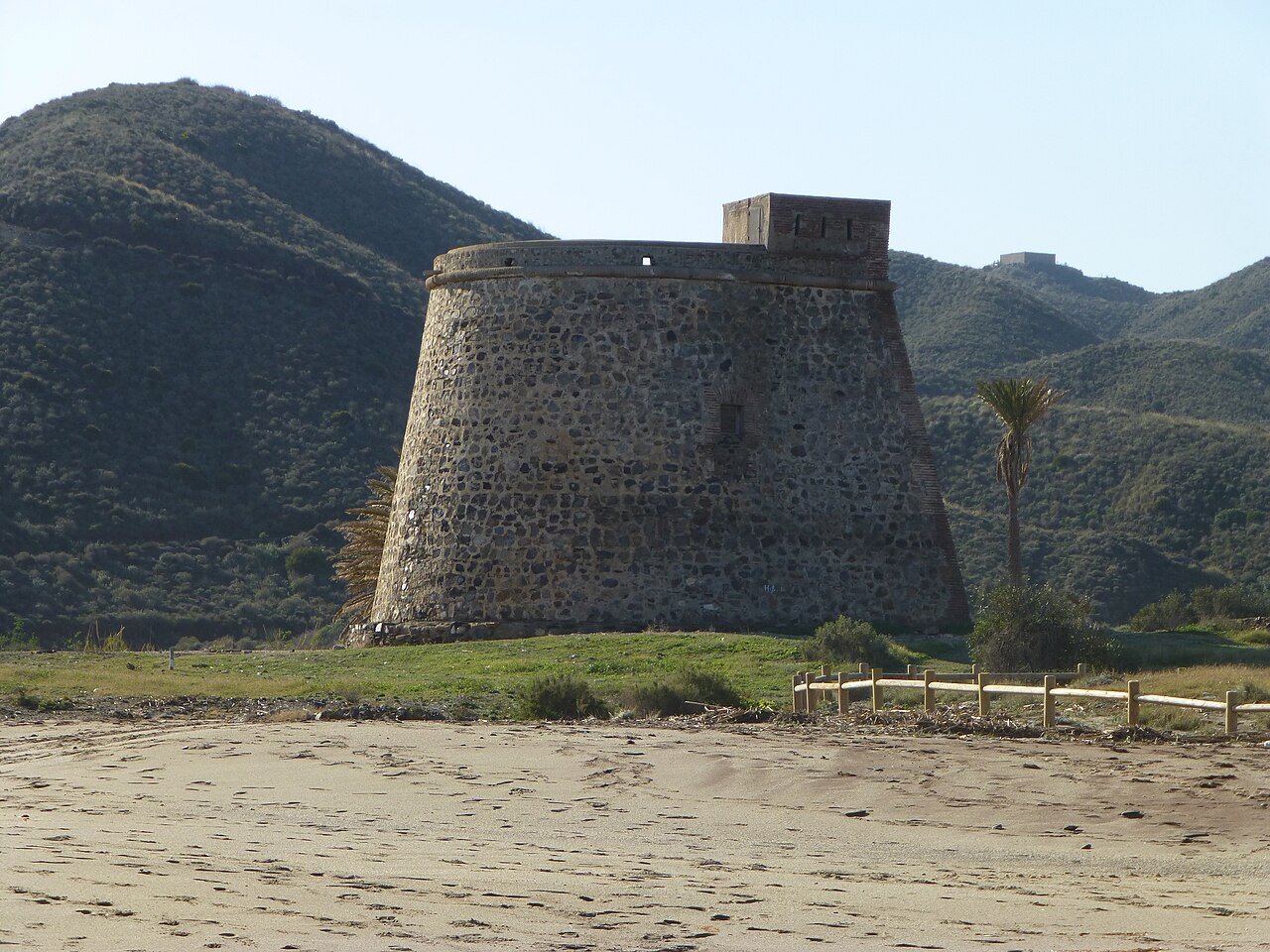 El Castillo de Macenas, torre de piedra sobre la playa, con Sierra Cabrera detrás